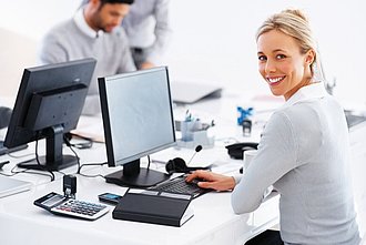 Eine Frau sitzt vor dem Computer und lächelt in die Kamera