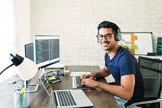 Ein Mann arbeitet am Computer und lächelt in die Kamera